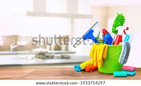 Cleaning items in a bucket on a wooden table infront of a kitchen background. Cleaning service concept with copy space