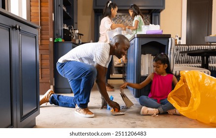 Cleaning kitchen floor, father and daughter picking up trash, mother and child in background. family, teamwork, household, chores, bonding, parenting - Powered by Shutterstock