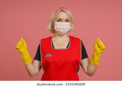 Cleaning Lady In An Apron, Gloves And A Protective Mask Shows Her Fists On A Colored Background