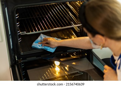 Cleaning lady in gloves washing oven in stylish kitchen. Close-up