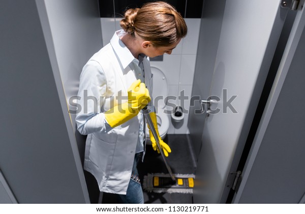 Cleaning lady or janitor mopping the floor in restroom\
cleaning the stall 