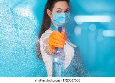 A Cleaning Lady In A Mask Disinfects A Blue Background.