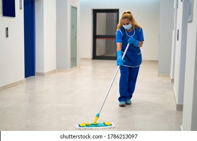 A cleaning lady with the mask on her face mops the floor in an office building