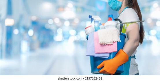 Cleaning Lady In A Protective Mask With A Bucket And Cleaning Products On A Blurred Background.