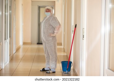 A Cleaning Lady In A Protective Suit During A Coronavirus Infection Stands In A Hospital Corridor.