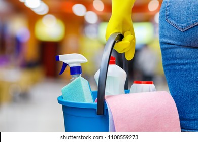 Cleaning lady standing with a bucket and detergents on blurred background.