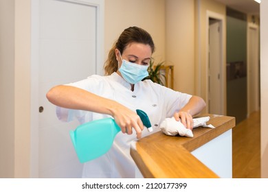 Cleaning Lady Using A Face Mask While Cleaning The Reception Desk Of A Spa Or Health Center.