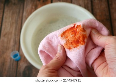 Cleaning laundry manually. Women's hands in gloves washing dirty stained on colored cloth with a stain remover and soak in soapy water, closeup - Shutterstock ID 2144547911