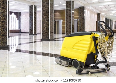Cleaning machine in empty office lobby, yellow vacuum equipment is on clean shiny marble floor in commercial building. Concept of professional cleaning, maintenance and care service.