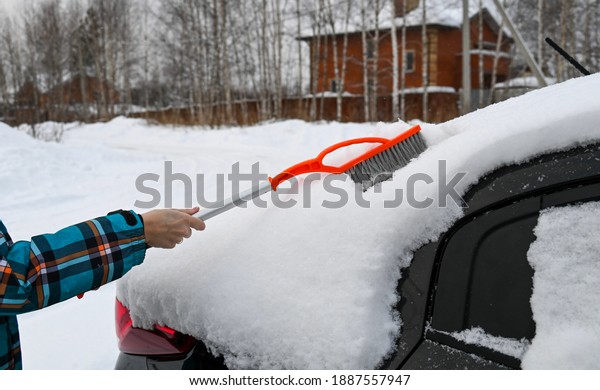 Cleaning the machine from snow with a brush. Woman\
cleans the trunk of a\
car