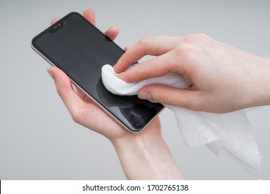 Cleaning Mobile Phone To Eliminate Germs, Coronavirus Covid-19. Woman Hands Cleaning Smartphone By Alcohol Hand Sanitizer And Wipe With Cloth.