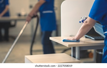 Cleaning an office table.Other cleaners clean in the background - Shutterstock ID 2227058019