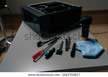 Cleaning open computer case with specialized tools like screwdrivers and brushes on gray table in workshop, ensuring optimal performance and preventing overheating, close-up, no people.