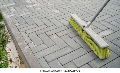  Cleaning Paving Stones With A Brush. The Gardener Cleans The Debris From The Paving Stones. Brushing Paving Stones With Sand, Sunny Day.