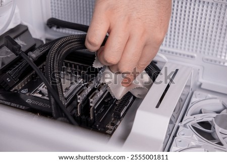 cleaning PC components with microfiber cloth, hand wiping RAM slots, inside computer case, hardware maintenance, dust removal, PC care, cleaning process, workstation