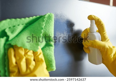 Cleaning process with yellow gloves: hands using cleaning spray and cloth for surface maintenance.