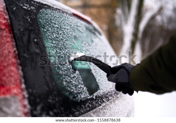 Cleaning the rear car\
window of snow with ice scraper before the trip. Man removes ice\
from car rear window wiper. Male hand cleans car with special tool\
at snowy winter day.