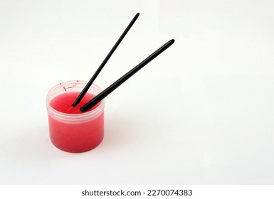 Cleaning red acrylic paint from paintbrushes by soaking in small container filled with water - Powered by Shutterstock