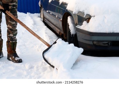 Cleaning The Road And The Area Around The Car On The Road From Snow. The Concept Of Cleaning The Car From Snow, Heavy Snowfall, Winter Storm, Storm Warning.