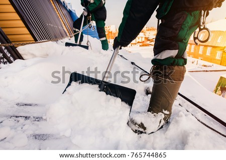 Cleaning roofs of buildings from snow, ice in the winter with a shovel.