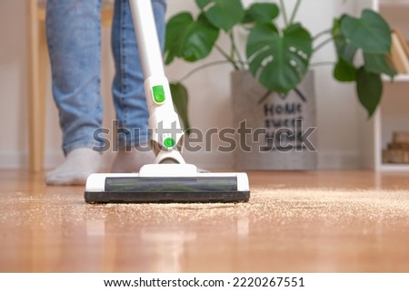 Cleaning room with modern wireless vacuum cleaner without cord. Man in jeans is cleaning floor with modern cordless vacuum cleaner without cord. Man removes sawdust from floor with vacuum cleaner.
