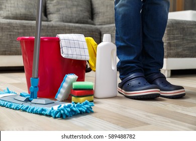 Cleaning service. Bucket with sponges, chemicals bottles and mopping stick. Rubber gloves, plunger and towel. Man standing in boating shoes.