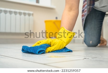 cleaning service. crop image of woman thoroughly and gently washing and cleaning white laminate floor. female hands in yellow gloves wipe wooden floor with blue microfiber cloth