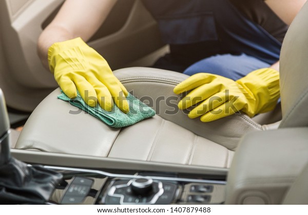 Cleaning service. Man in uniform and yellow gloves\
washes a car interior in a car wash. Worker washes the chairs of\
the leather salon