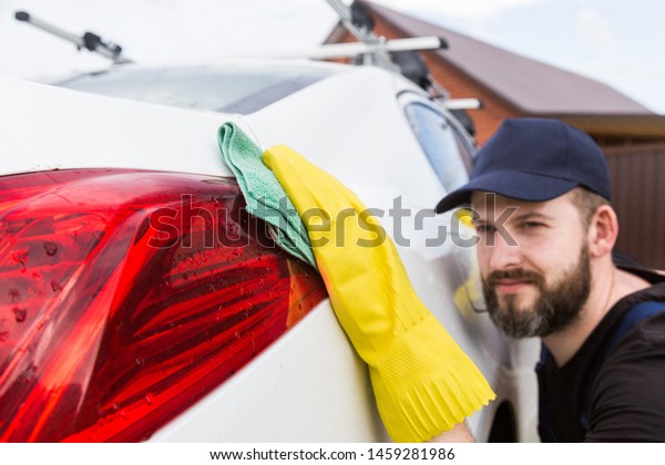 Cleaning service. Man in uniform and yellow\
gloves washes a car body in a car\
wash