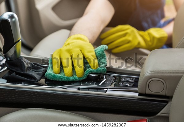 Cleaning service. Man in uniform and yellow
gloves washes a car interior in a car
wash