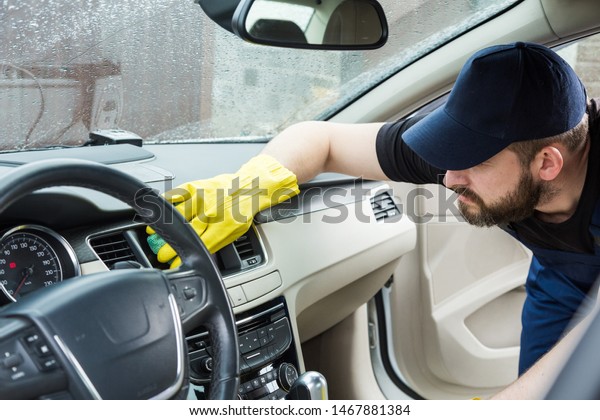 Cleaning service. Man in uniform and yellow
gloves washes a car interior in a car
wash