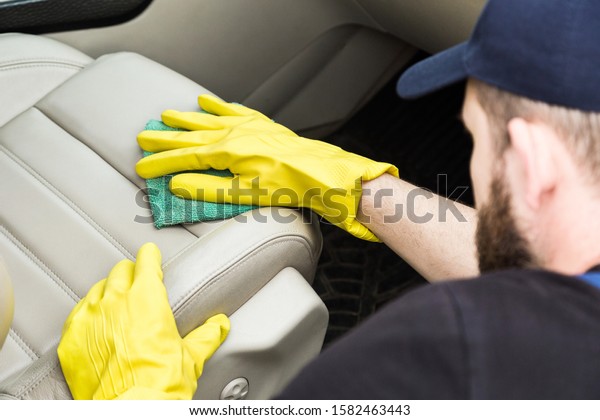Cleaning service. Man in uniform and yellow\
gloves washes a car interior in a car\
wash
