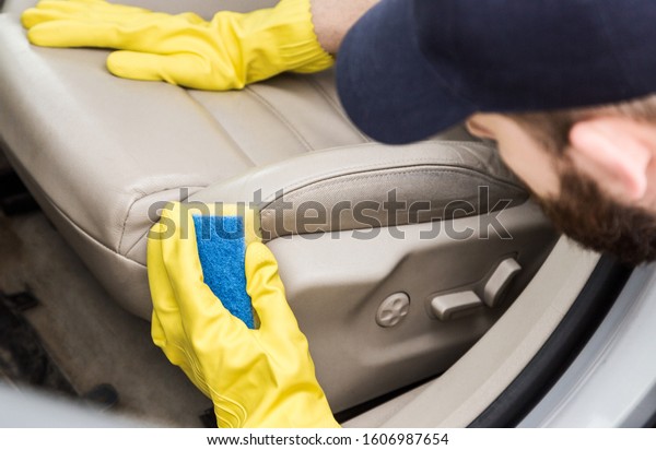 Cleaning service. Man in uniform and yellow gloves
washes a car interior in a car wash. Worker washes the chairs of
the leather salon