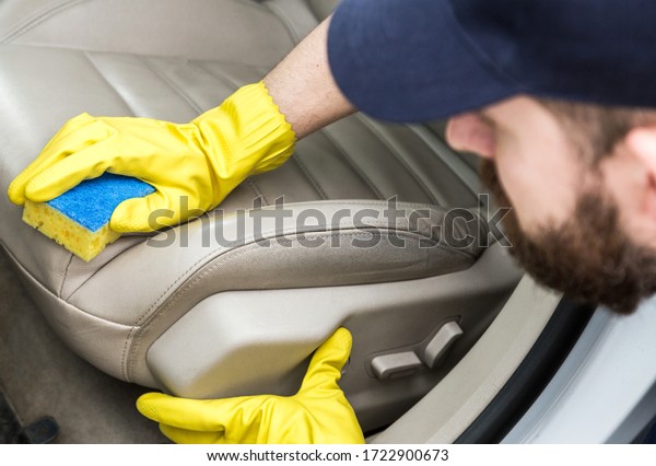 Cleaning service. Man in uniform and yellow gloves\
washes a car interior in a car wash. Worker washes the chairs of\
the leather salon