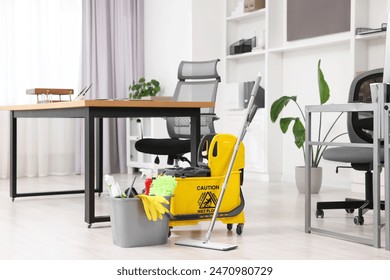 Cleaning service. Mop, bucket with supplies and wet floor sign in office - Powered by Shutterstock