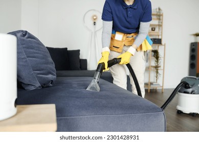 Cleaning service worker vacuuming sofa from dust with vacuum cleaner during housework