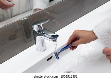 Cleaning shaving razor in bathroom sink. Rinsing off razor with water.