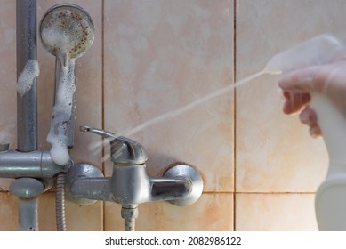 Cleaning the shower. A gloved hand holds an anti-limescale and anti-rust agent. Spraying cleaning agent onto the surface of the faucet and pipe