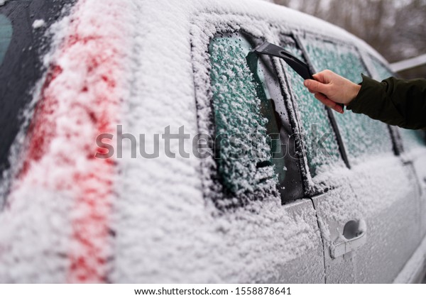 Cleaning the side car\
windows of snow with ice scraper before the trip. Man removes ice\
from car windows. Male hand cleans car with special tool at snowy\
frosty winter day.