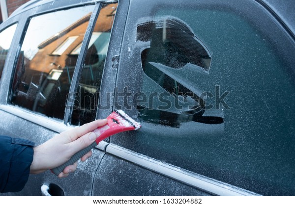 Cleaning the\
side car windows of snow with ice scraper before the trip. Man\
removes ice from car windows. A male\
hand.