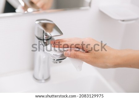 Cleaning the sink faucet with a microfiber cloth. Cleaning the bathroom. Sanitize surfaces prevention in hospital and public spaces against corona virus. Woman hand using wet wipe.