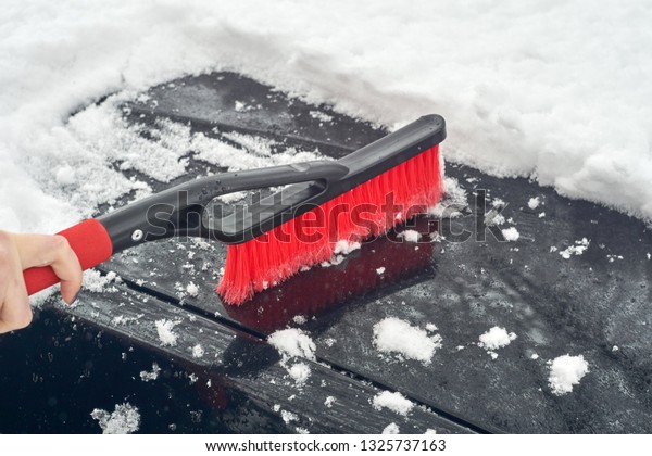 Cleaning snow off the car: Red snow brush and piles\
of snow on the black car\
hood.