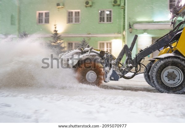 Cleaning snow from road. Closeup shot of\
snowplow tractor on city street blow snow for transport and traffic\
safety. Workers work after blizzard storm. Municipal utilities and\
equipment for\
wintertime