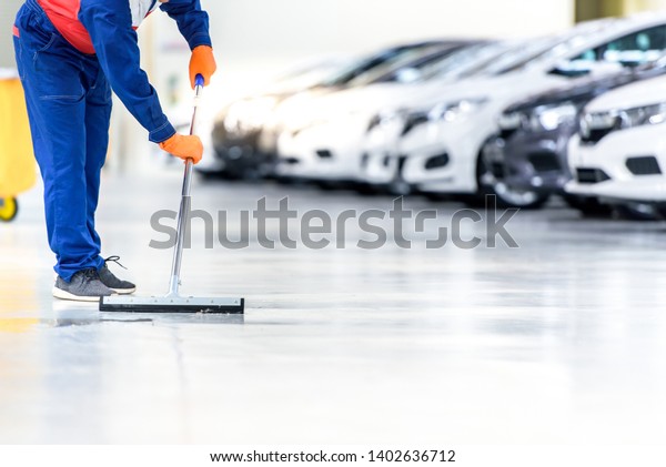 The cleaning staff is cleaning on the work area\
that is the epoxy floor. In a car repair shop or service center The\
background is a new car park waiting to be sold. ,Car industry on\
the epoxy floor