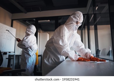 Cleaning staff in protective gear disinfecting the office workplaces - Powered by Shutterstock