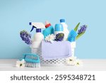 Cleaning supplies with spring flowers on table against blue background