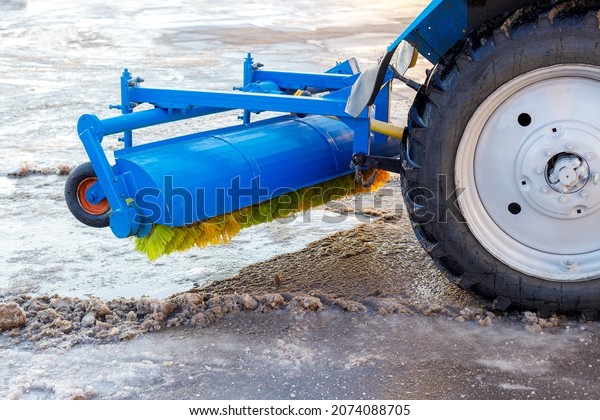 Cleaning and sweeping streets from\
snow. Tractor with new hinged brush clears area.\
Close-up.