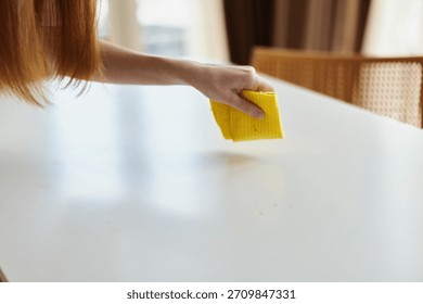 Cleaning table with yellow sponge and hand wiping white surface in bright kitchen, closeup of household chore and surface maintenance for hygiene, tidy home routine.