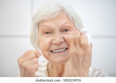 Cleaning teeth. Gray-haired woman cleaning her teeth and using floss - Shutterstock ID 1903119976