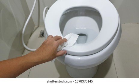 Cleaning Toilet Seat By Using Tissue Paper.Human's Hand Wipe The Toilet Seat Cover Clean With Tissue Paper. 